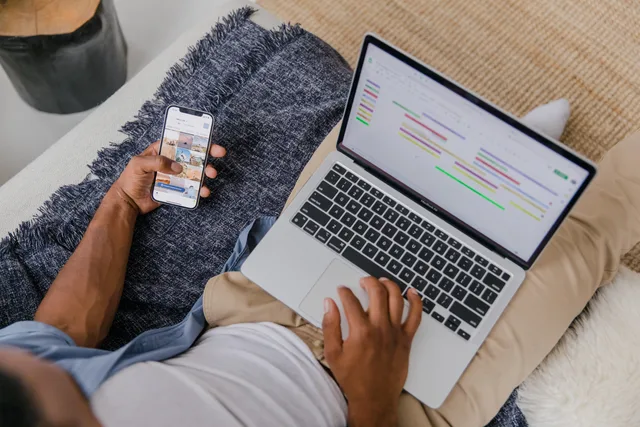 Man multitasking with phone and laptop on sofa, showcasing modern remote work lifestyle. Social media manager certification UK: which qualification do employers want?