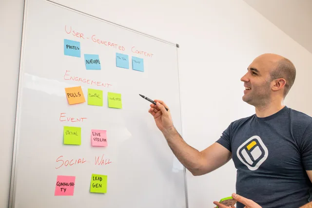 Smiling man presents strategies on a whiteboard with post-its, focusing on engagement and user-generated content. Social media training market size in England: no official total, and what ESS, ONS and DBT data can show