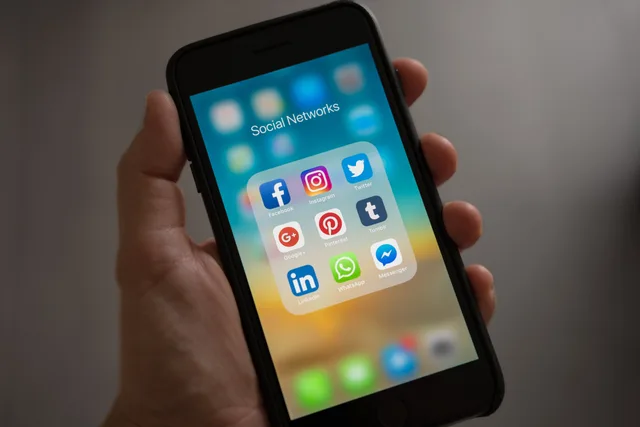 A smartphone displaying various social media icons held in a hand, showcasing modern communication apps. Five social media training risk scenarios to rehearse