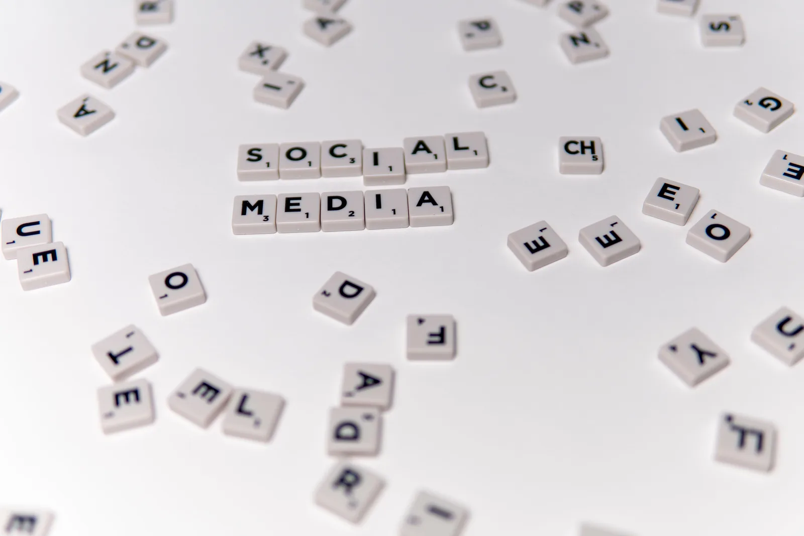 White Scrabble tiles forming the phrase 'social media' on a scattered background.