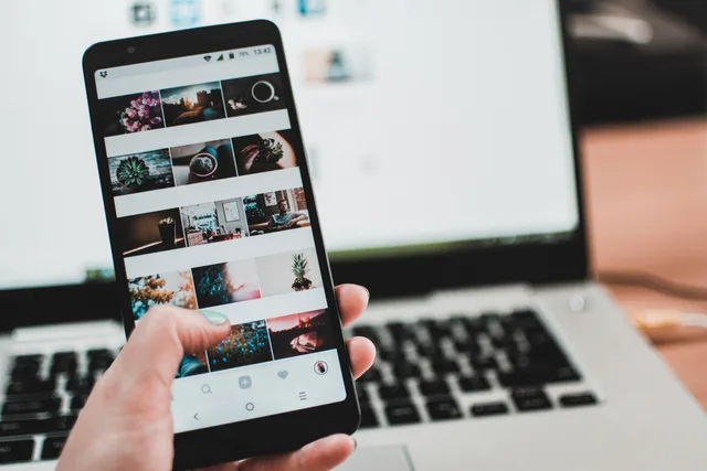 A person uses a smartphone to browse social media in front of a laptop, emphasizing modern technology and lifestyle. A social media training strategy that starts with the job, not the course catalogue