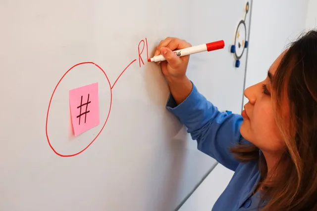 Focused woman writing on a whiteboard with marker, emphasizing hashtag concept. Social media training UK regulations: who owns each?