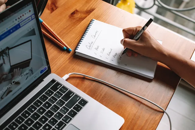 A person writing notes while researching online courses on a laptop in a home setting. TikTok marketing course UK: four tests to judge if it is worth it